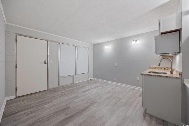 Unfurnished living room with a sink, light wood finished floors, a textured ceiling, and baseboards | Image 7