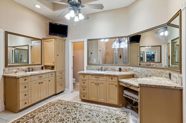 This luxurious primary bathroom provides abundant counter and cabinet space for storing lotions and potions. Classic granite counters and warm travertine tile flooring are accented with bronze hardware and Rohl faucets for a timeless finish. | Image 18