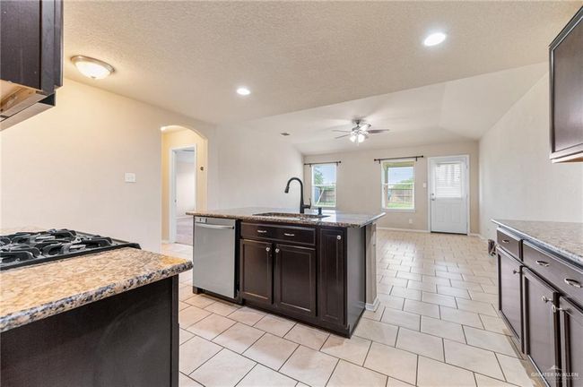 Kitchen featuring stainless steel dishwasher, gas cooktop, a ceiling fan, arched walkways, and a kitchen island with sink | Image 5