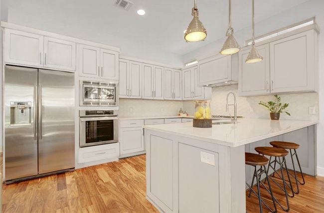Kitchen featuring a kitchen bar, visible vents, a sink, a peninsula, and built in appliances | Image 12