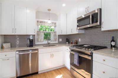 Kitchen featuring tasteful backsplash, stainless steel appliances, pendant lighting, white cabinets, and light hardwood / wood-style flooring | Image 3