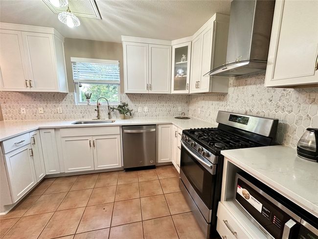 Kitchen featuring appliances with stainless steel finishes, wall chimney range hood, light tile patterned floors, and white cabinetry | Image 7