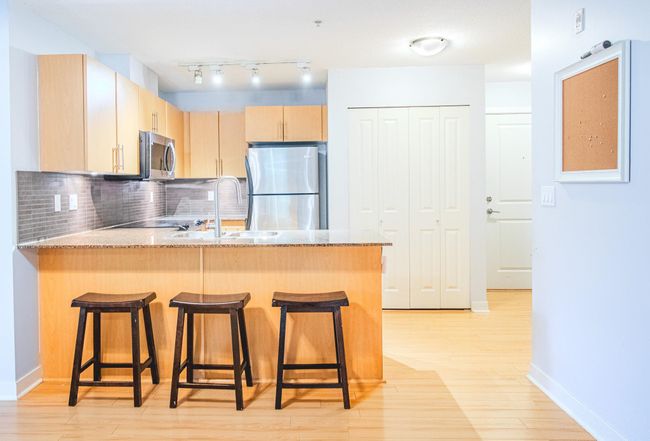 Kitchen featuring appliances with stainless steel finishes, a peninsula, light brown cabinetry, backsplash, and light wood finished floors | Image 5
