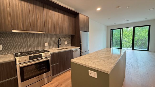 Kitchen featuring modern cabinets, appliances with stainless steel finishes, light countertops, a kitchen island, and backsplash | Image 13