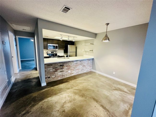 Kitchen with unfinished concrete floors, a textured ceiling, stainless steel appliances, light countertops, and pendant lighting | Image 7