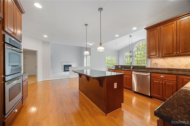 Kitchen with a breakfast bar, light wood-style floors, appliances with stainless steel finishes, double ovens, a glass covered fireplace, and open floor plan | Image 14