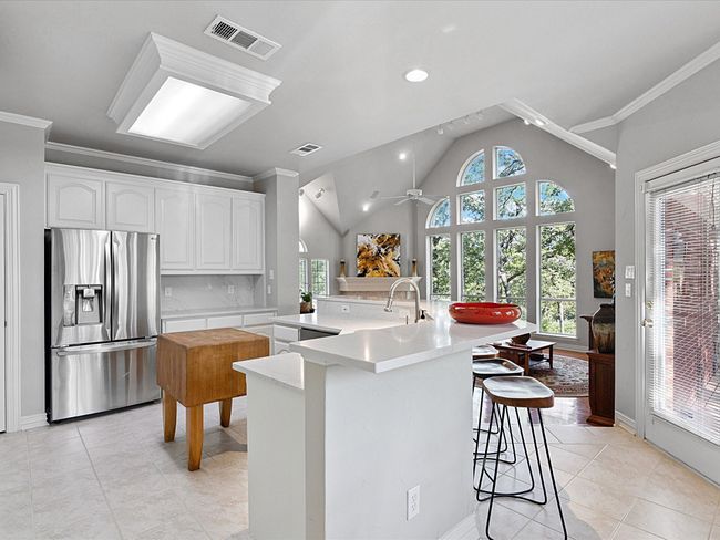Kitchen with stainless steel fridge with ice dispenser, light tile patterned floors, plenty of natural light, crown molding, and vaulted ceiling | Image 12