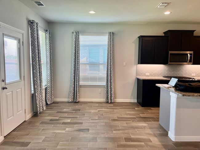Kitchen featuring stainless steel microwave, backsplash, light wood finished floors, recessed lighting, and light stone countertops | Image 6
