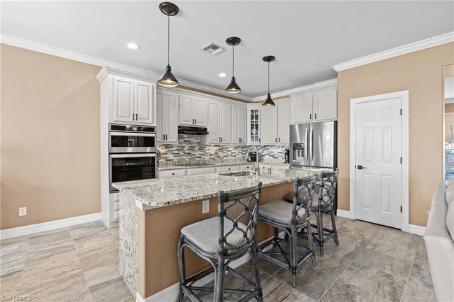 Kitchen with appliances with stainless steel finishes, a sink, under cabinet range hood, crown molding, and backsplash | Image 19