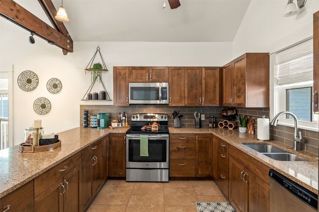 Kitchen with stainless steel appliances, tasteful backsplash, a peninsula, light stone countertops, and beamed ceiling | Image 12