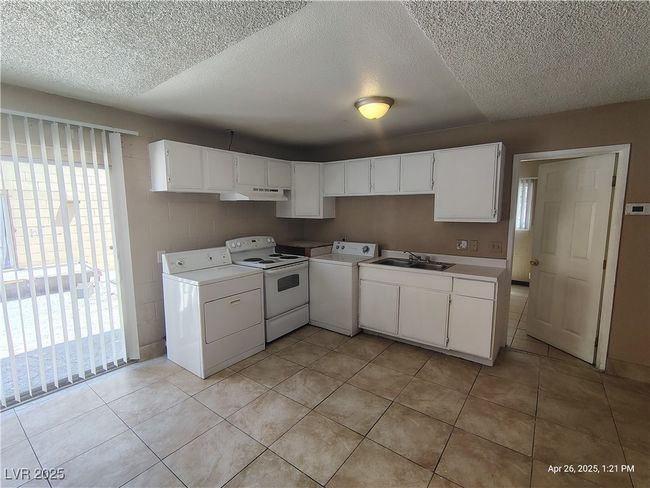 Kitchen featuring a textured ceiling, a sink, washer / dryer, and under cabinet range hood | Image 5