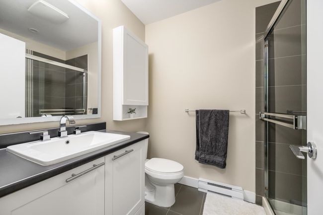 Bathroom featuring tile patterned flooring, a shower stall, baseboard heating, toilet, and vanity | Image 13