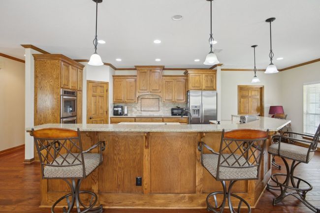 Kitchen featuring dark wood-style flooring, ornamental molding, backsplash, light stone counters, and appliances with stainless steel finishes | Image 5