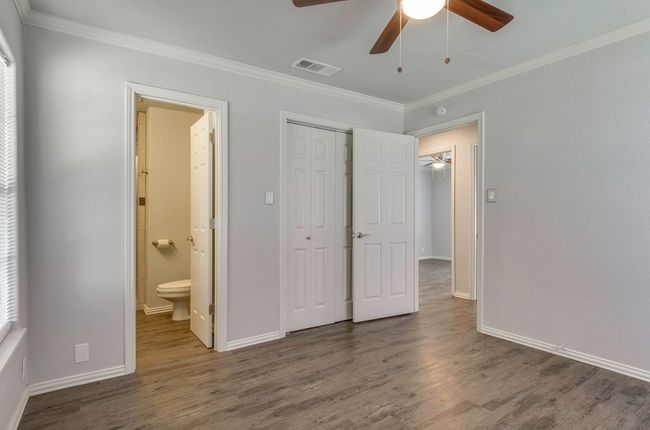Unfurnished bedroom featuring crown molding, dark wood-style floors, a closet, connected bathroom, and ceiling fan | Image 22