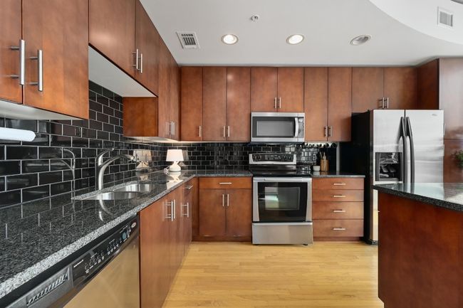 Kitchen with stainless steel appliances, light wood finished floors, a sink, dark stone counters, and decorative backsplash | Image 5