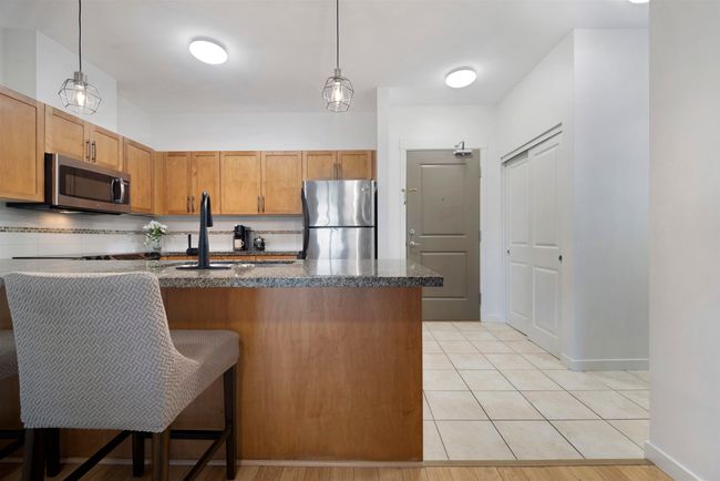 Kitchen featuring light tile patterned floors, a kitchen breakfast bar, pendant lighting, and appliances with stainless steel finishes | Image 7