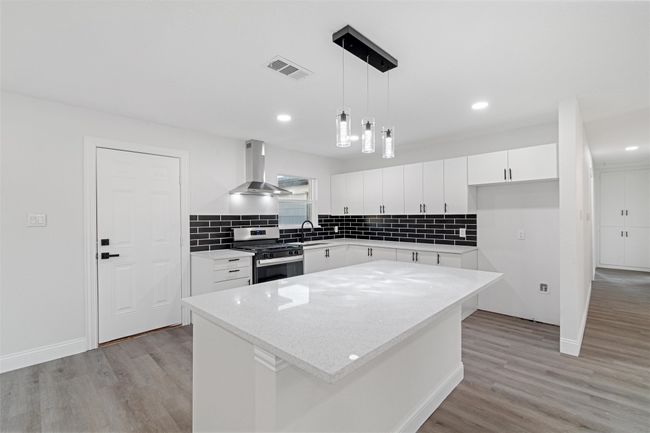 Kitchen with white cabinets, stainless steel gas stove, wall chimney exhaust hood, and a center island | Image 9