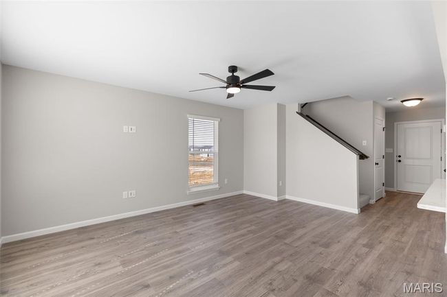 Unfurnished living room featuring a ceiling fan, wood finished floors, baseboards, and stairway | Image 6