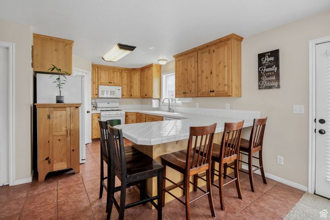 Kitchen with white appliances, a peninsula, tile counters, and light tile patterned floors | Image 5