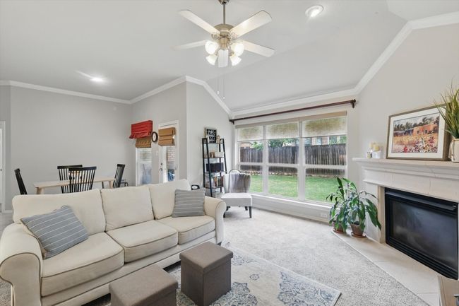 Living area featuring crown molding, light colored carpet, a ceiling fan, vaulted ceiling, and a premium fireplace | Image 20