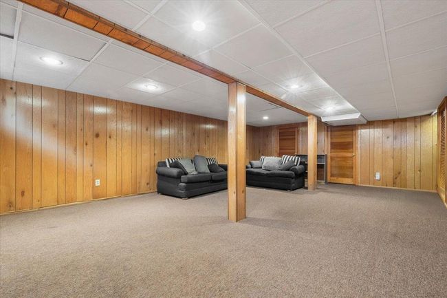 Carpeted living area featuring wooden walls, a drop ceiling, and recessed lighting | Image 24