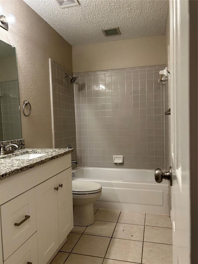Bathroom with a textured ceiling, vanity, shower / washtub combination, tile patterned flooring, and a textured wall | Image 15