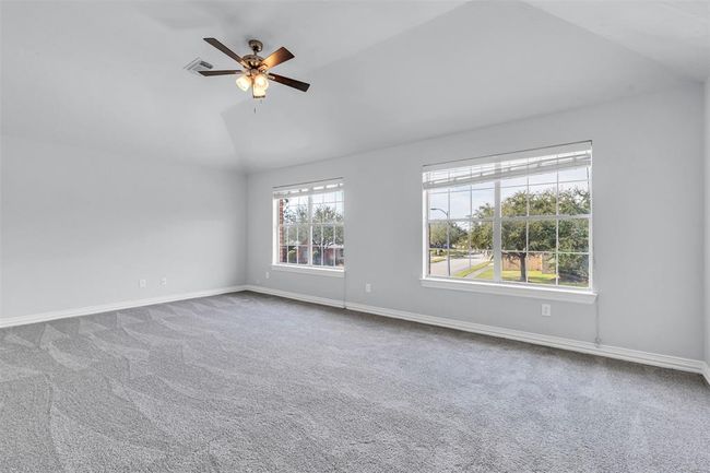 Spacious, well-lit room with large windows, fresh gray carpet, and a ceiling fan. Perfect for a bedroom or office space with a pleasant view of greenery outside. | Image 40