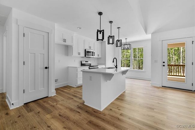 Kitchen with light wood finished floors, an island with sink, a sink, stainless steel appliances, and white cabinetry | Image 11