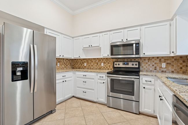 Kitchen featuring stainless steel appliances, crown molding, decorative backsplash, light stone counters, and white cabinets | Image 13