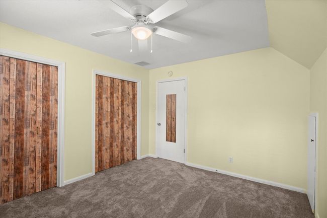 This room features soft yellow walls, plush carpet, a ceiling fan, and ample closet space with wood-textured doors, ideal for a cozy bedroom setup. | Image 35
