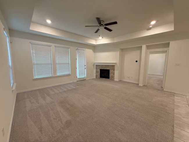 Unfurnished living room featuring a tray ceiling, ceiling fan, a fireplace, light colored carpet, and recessed lighting | Image 26