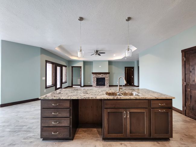 Kitchen with a ceiling fan, dark brown cabinetry, light wood-style floors, a fireplace, and a tray ceiling | Image 5
