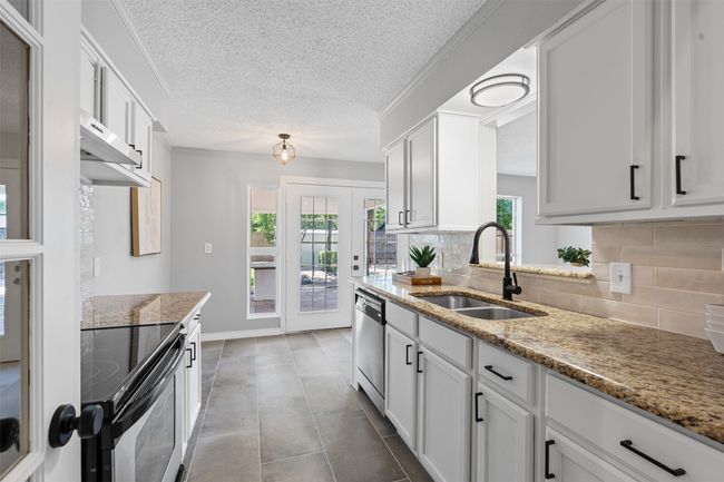 Kitchen with stainless steel appliances, decorative backsplash, white cabinets, light stone counters, and a textured ceiling | Image 13