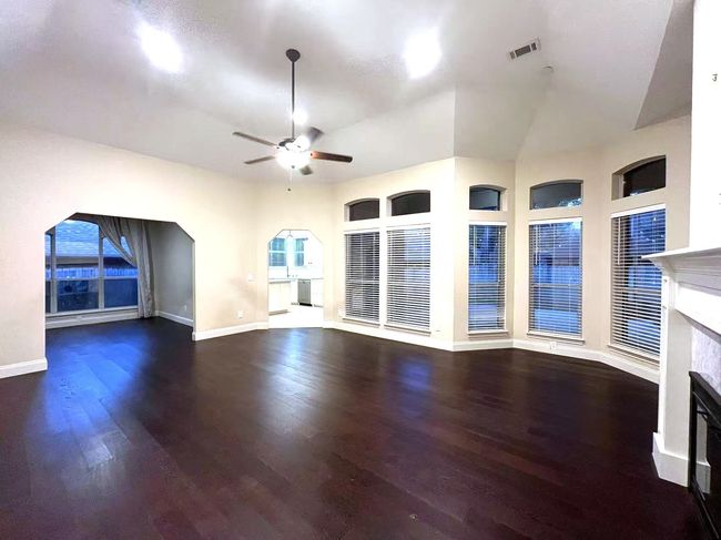 Unfurnished living room with a premium fireplace, ceiling fan, wood finished floors, and arched walkways | Image 20