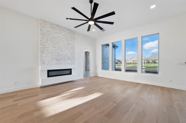 Unfurnished living room featuring a ceiling fan, a stone fireplace, baseboards, and light wood finished floors | Image 12