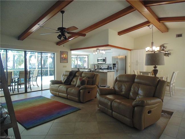 Living area featuring visible vents, vaulted ceiling with beams, ceiling fan with notable chandelier, and light tile patterned flooring | Image 12