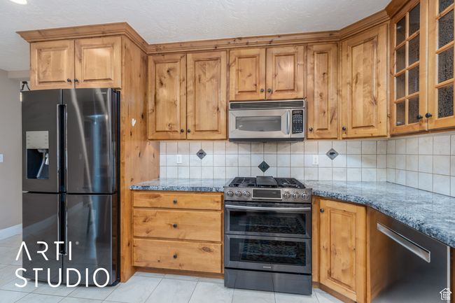 Kitchen featuring stone countertops, light tile patterned floors, decorative backsplash, and appliances with stainless steel finishes | Image 21