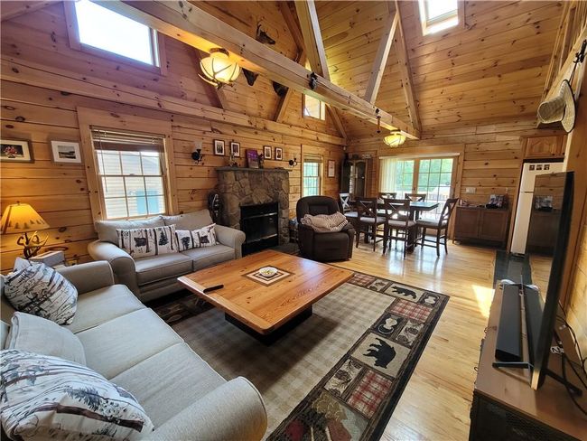 Living room with a stone fireplace, light hardwood / wood-style floors, wood walls, and beamed ceiling | Image 5
