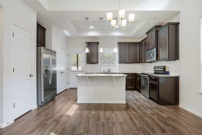 Kitchen with a tray ceiling, dark brown cabinetry, stainless steel appliances, and dark wood-style floors | Image 6