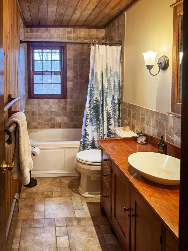 Full bath with toilet, wood ceiling, vanity, tile walls, and shower / bathtub combination with curtain | Image 16