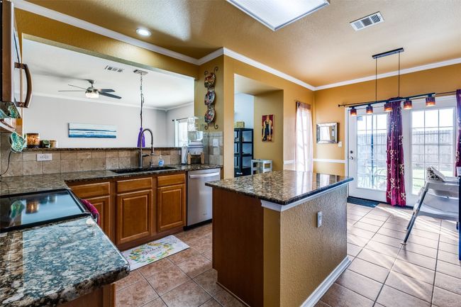 Kitchen with stainless steel dishwasher, a sink, brown cabinetry, tile patterned floors, and crown molding | Image 10