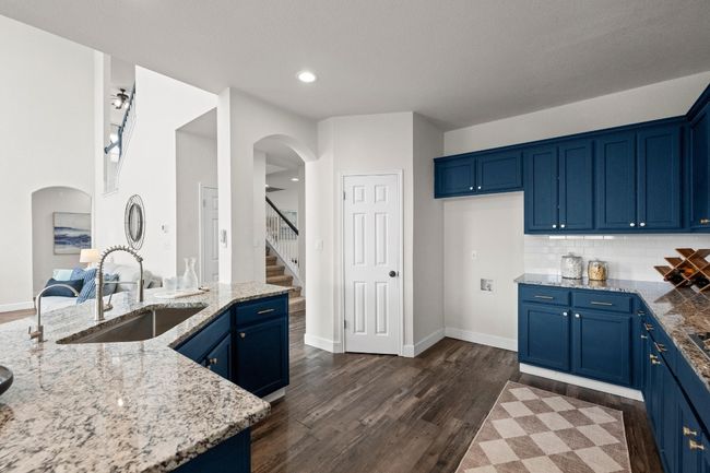 Kitchen featuring a sink, blue cabinetry, light stone countertops, dark wood-style flooring, and arched walkways | Image 9