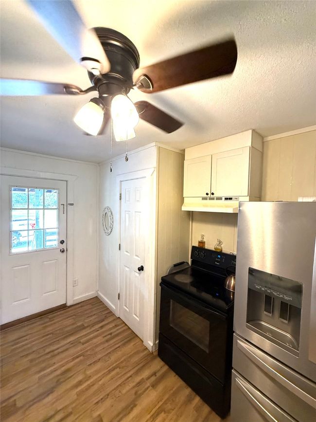Kitchen featuring stainless steel refrigerator with ice dispenser, black / electric stove, light wood-type flooring, ceiling fan, and a textured ceiling | Image 17