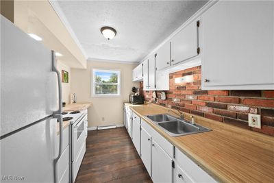 Kitchen with sink, white cabinets, white appliances, baseboard heating, and dark hardwood / wood-style flooring | Image 3