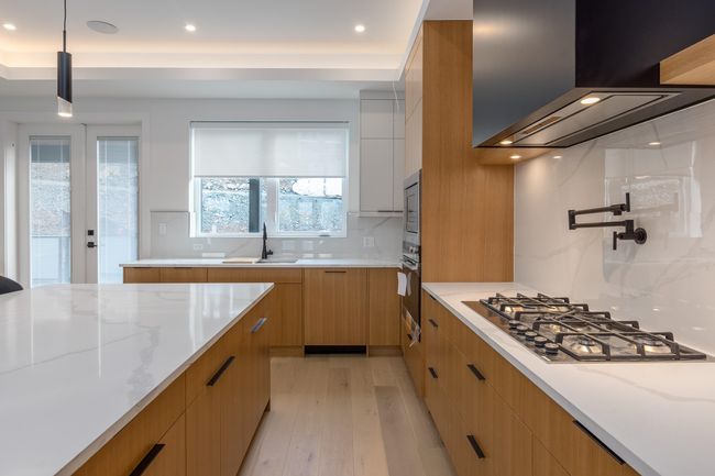 Kitchen featuring light stone counters, wall chimney exhaust hood, modern cabinets, and stainless steel appliances | Image 5