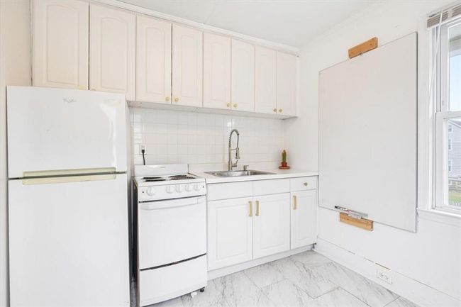 Kitchen with white cabinetry, white appliances, light tile patterned floors, backsplash, and sink | Image 15