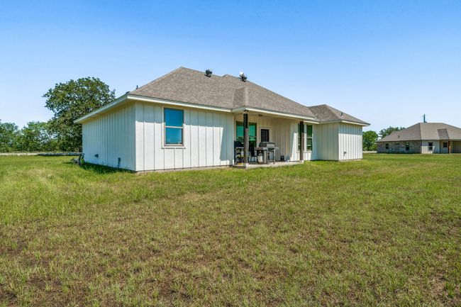 Rear view of property with board and batten siding, a patio, a lawn, and roof with shingles | Image 24