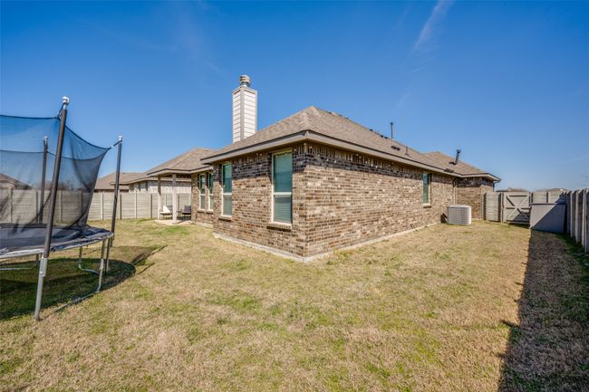 View of yard featuring central air condition unit, a trampoline, a fenced backyard, and a gate | Image 33