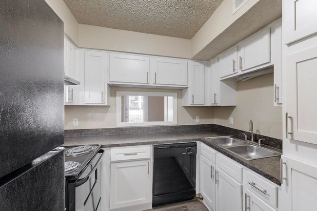 Kitchen with black appliances, a sink, dark countertops, a textured ceiling, and white cabinets | Image 19