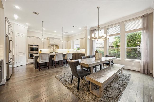 This spacious kitchen and dining area features modern cabinetry, stainless steel appliances, and a large island with seating. There is abundant natural light from large windows, creating a bright and inviting atmosphere. | Image 7